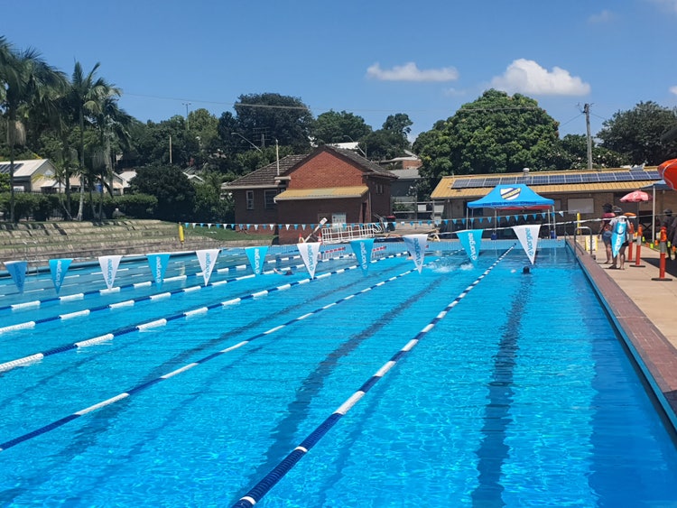 A clear blue pool with black racing lines is crossed by blue and white flags in the foreground of the photograph.