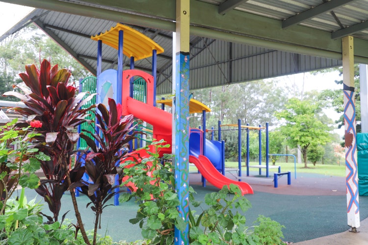 A colourful children's slide and playground in the backdrop under a covered play area, with garden in foreground.