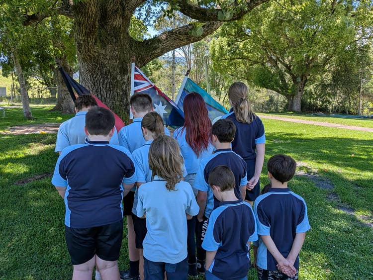Students face The Australian flag, Aboriginal Flag and Torres Strait Islander flag with their heads down in solemn recognition of fallen soldiers durng Remembrance Day.